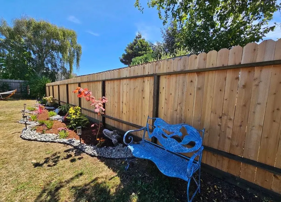 New cedar privacy fence behind a rock-bordered planting bed and a blue garden bench