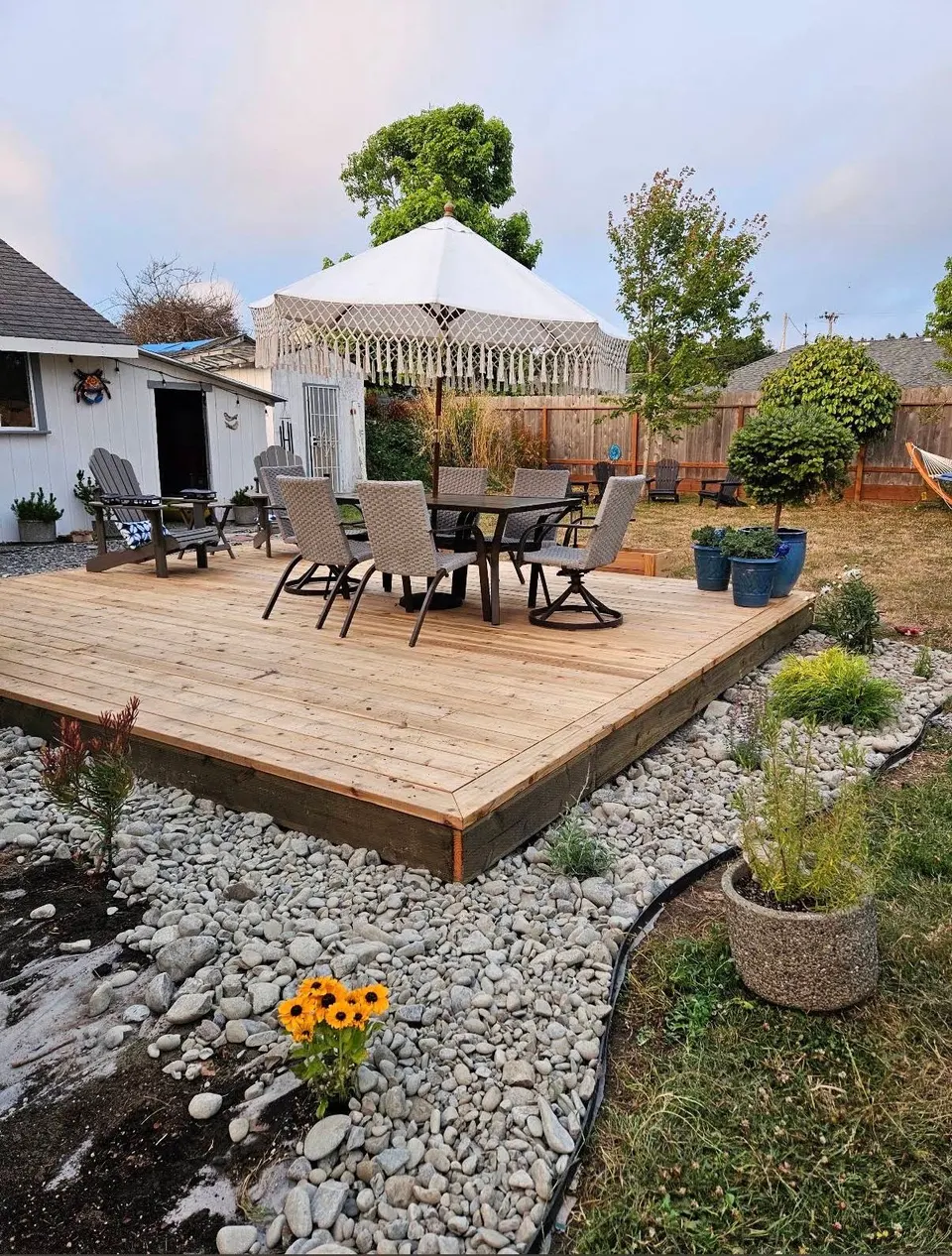New wood platform deck with outdoor dining set, wrapped by a river-rock border and fresh plantings