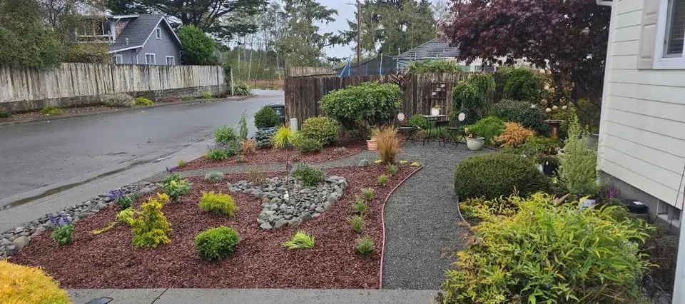 Corner-lot front yard with fresh mulch beds, a river-rock feature, and new plantings