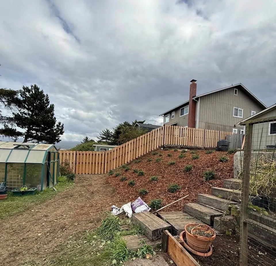 New wood fence stepping up a hillside above fresh mulch and young plantings on the slope