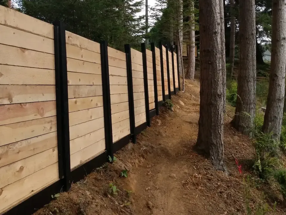 Horizontal-board wood fence with black steel posts along a forested hillside