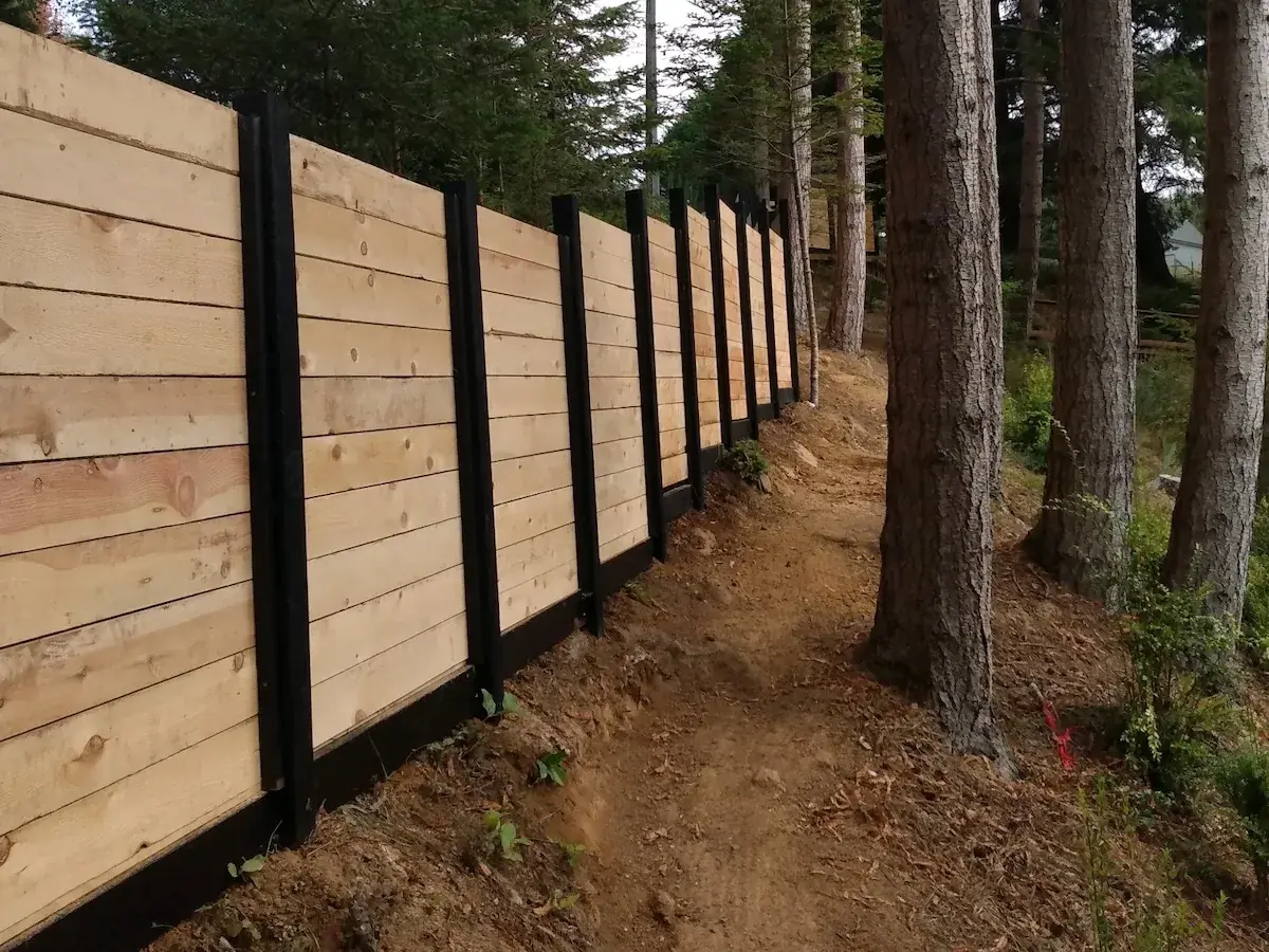 Horizontal-board wood fence with black steel posts along a forested hillside