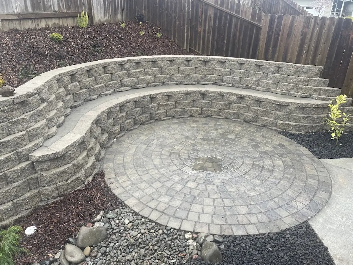 Circular paver patio wrapped by a curved block seating wall with fresh mulch beds