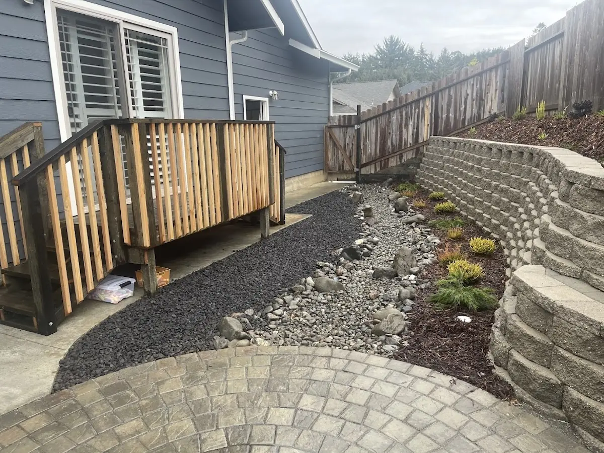 Curved block retaining wall above a dry-creek drainage bed and paver path