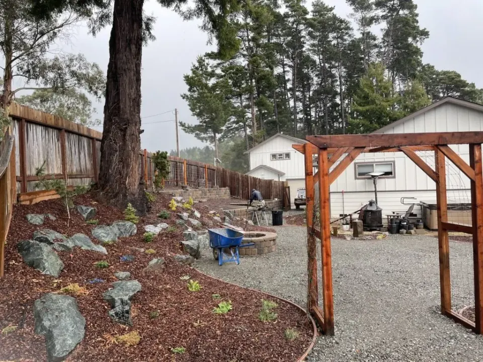 Redwood arbor framing a gravel patio with a paver fire pit and boulder planting beds