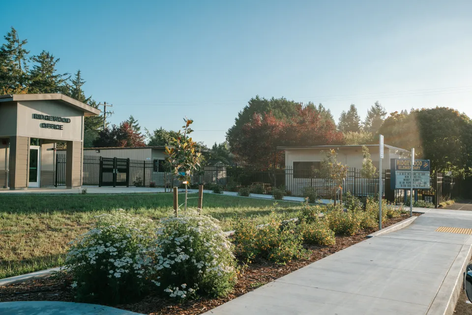 Concrete walkway curving past new shrub plantings and bark beds