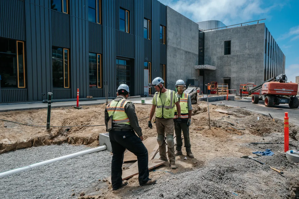 Deep Roots crew grading base rock by hand outside a commercial building under construction