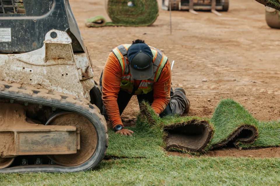 Crew member kneeling to set a strip of sod by hand against the finished edge