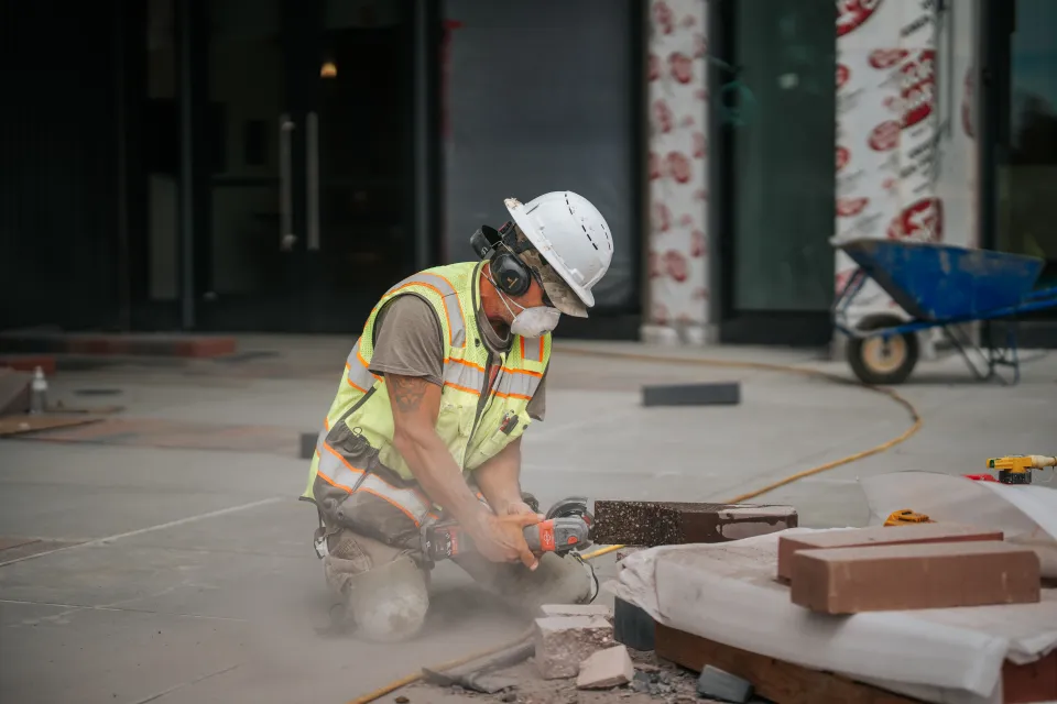 Crew member cutting a paver with a saw while setting a commercial walkway