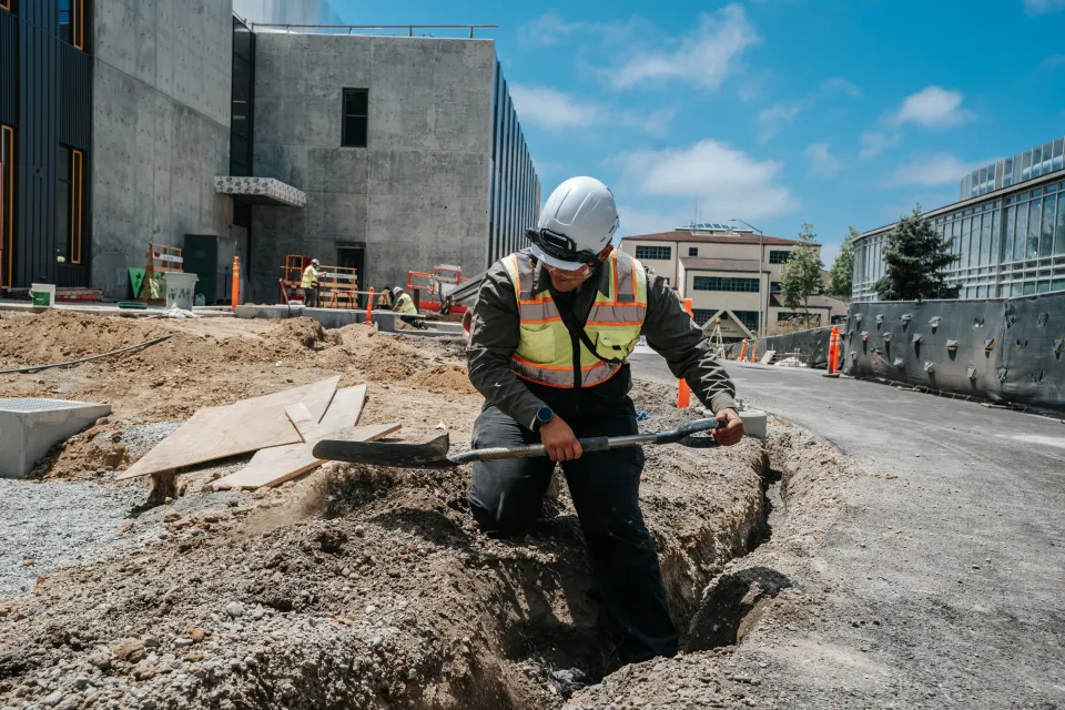 Crew member hand-digging a trench beside a new concrete walkway