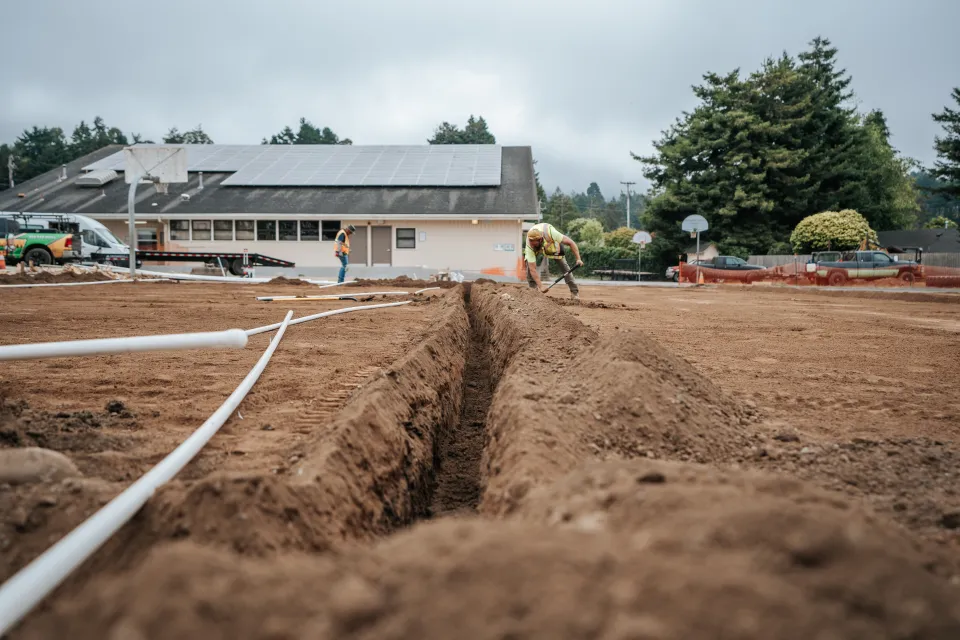 Irrigation mainline pipe laid out beside an open trench on a school site