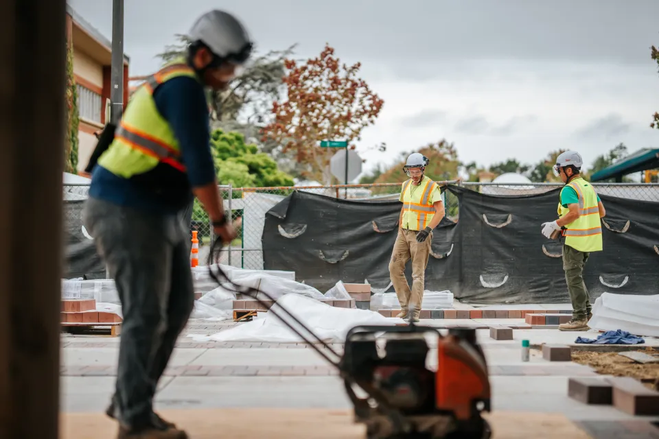 Crew member running a plate compactor to compact base material before paving
