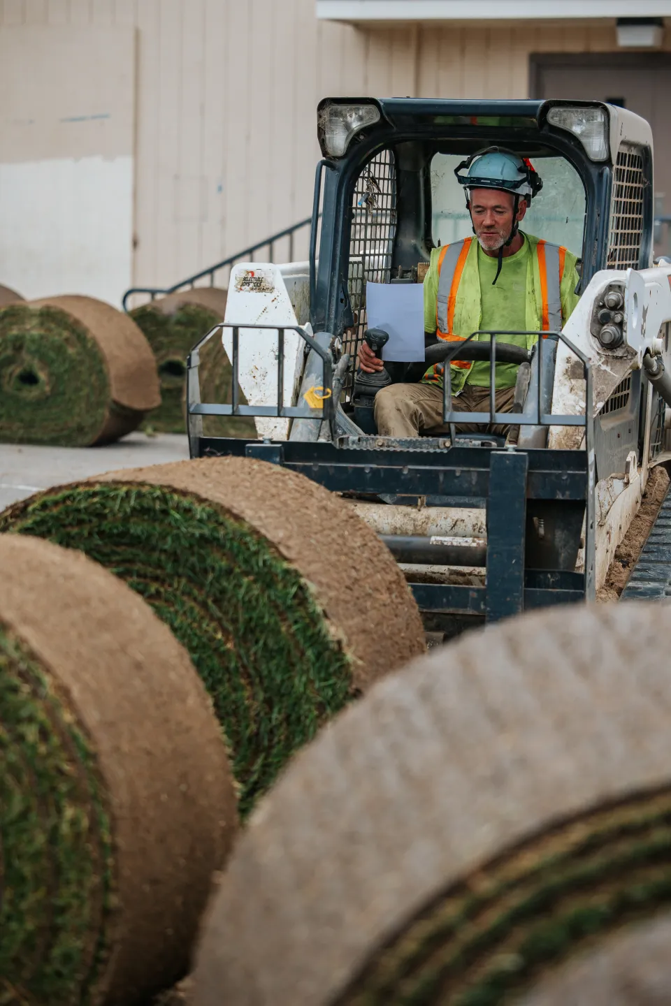 Operator running a compact track loader fitted with a sod roller