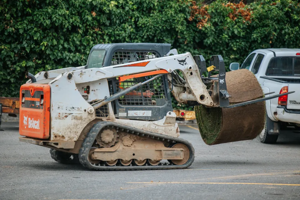 Compact track loader carrying a large sod roll on a sod roller attachment