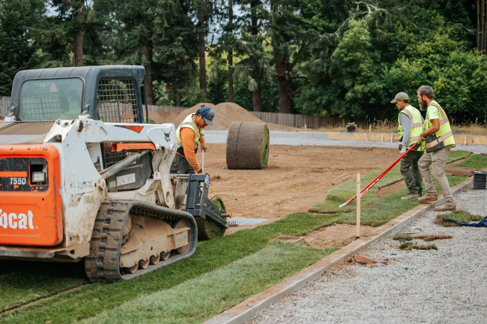 Landscaping crew installing sod along a gravel path on school grounds
