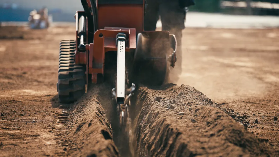 Close view of a trencher cutting a clean trench through dry soil