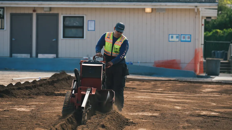 Operator running a walk-behind trencher across a graded jobsite